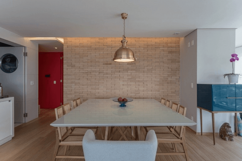 Sala de jantar, com parede de tijolos. À esquerda, porta colorida vermelha