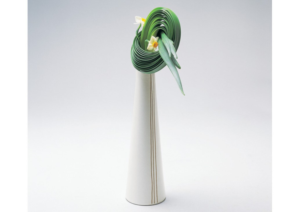 Ikebana moderno com vaso geométrico e folhas amarradas de forma circular