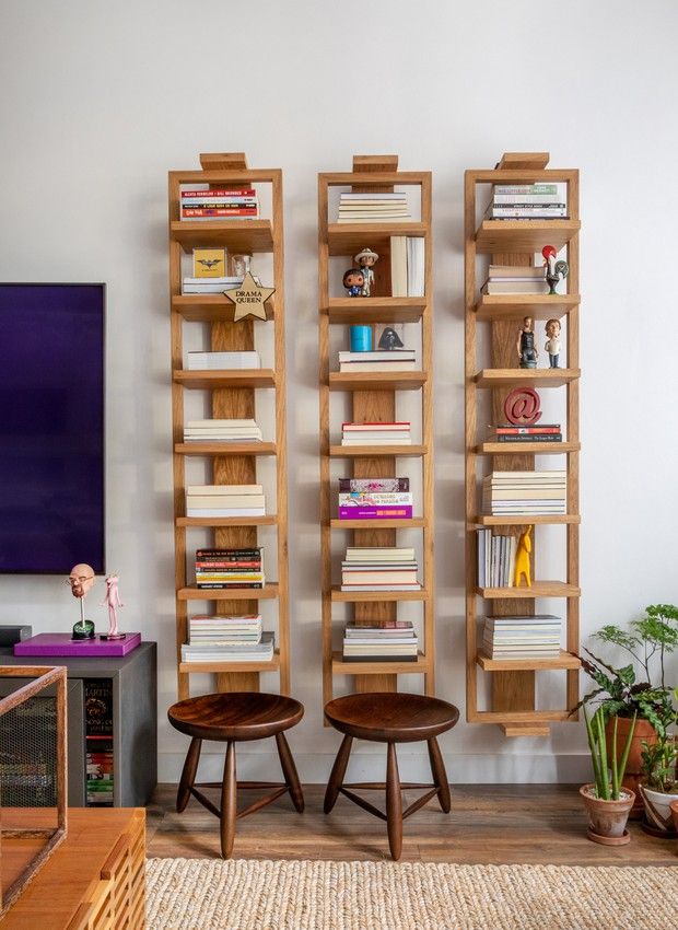Três estantes estreitas em madeira. Livros e bonequinhos nas prateleira