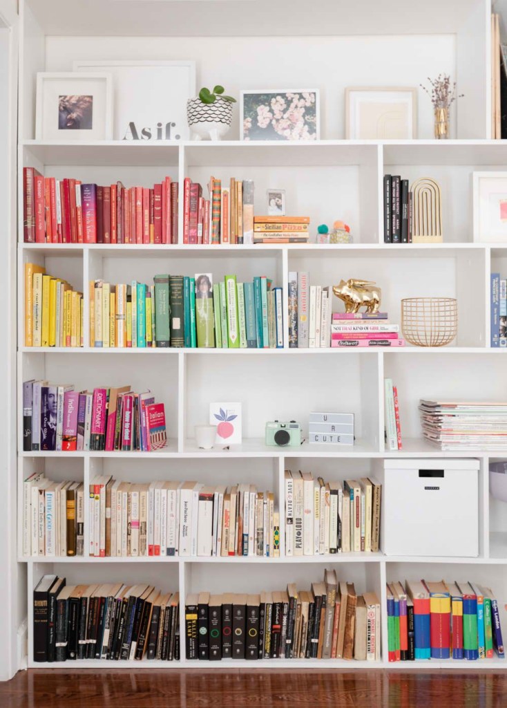 Estante branca com nichos e livros organizados por cor