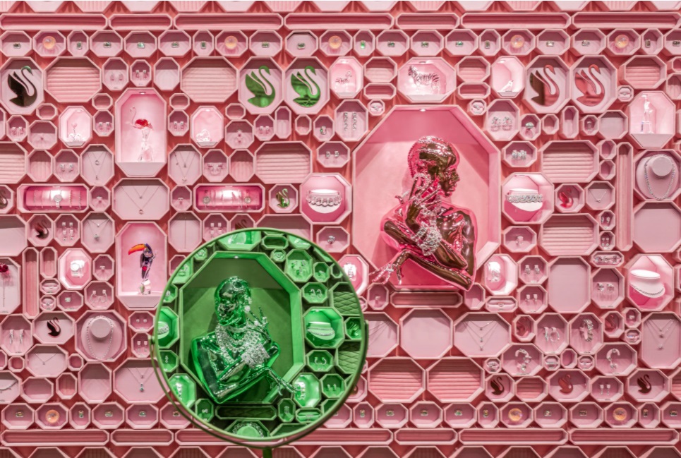 Parede coberta com caixas octogonais rosas. Espelho no canto inferior esquerdo reflete a parede verde do lado oposto.