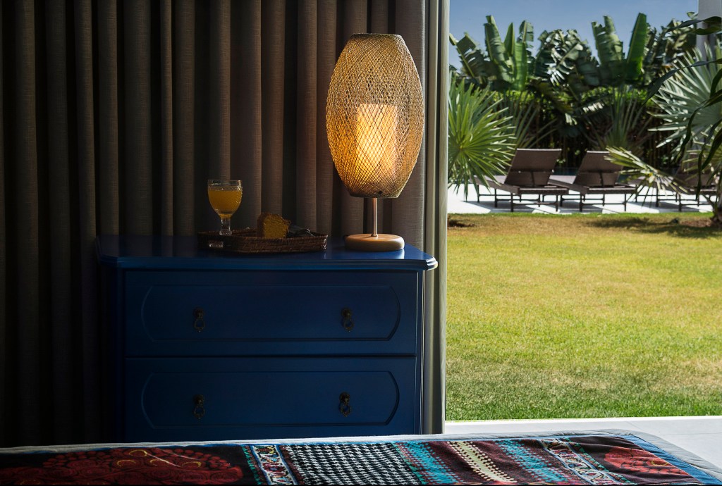 Sala com vista para campo, com abajur com cupula vazada dourada, sobre móvel de madeira azul