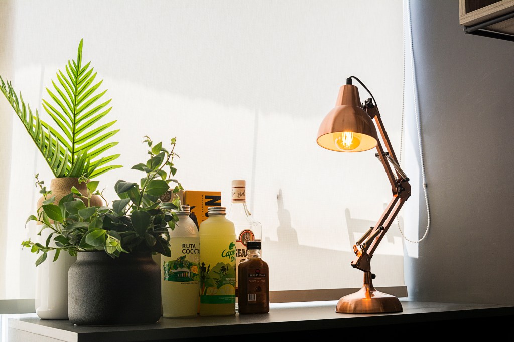Luminária de mesa flexível na cor cobre sobre mesa com bebidas e plantas