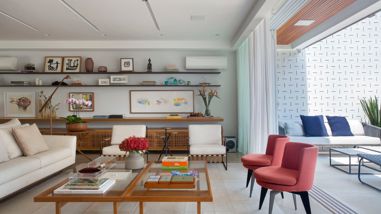 Sala de estar com mesa de centro, duas poltronas vermelhas, sofá branco e varanda integrada