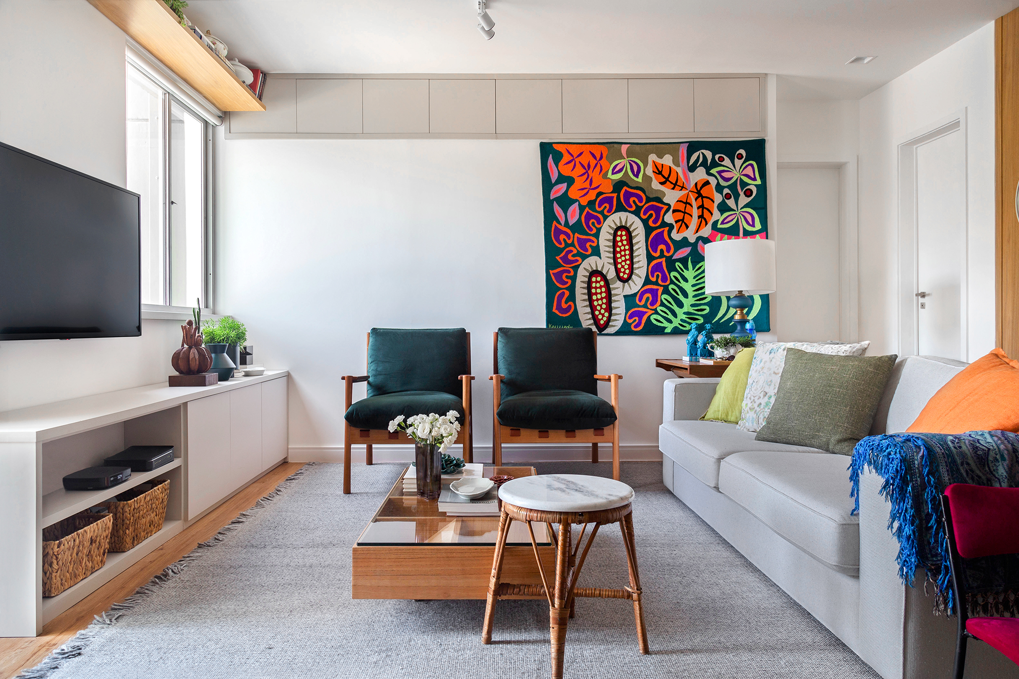Sala de estar com sofá de cor neutra, duas cadeiras e tapeçaria de parede ao fundo