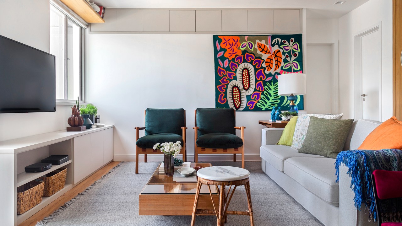 Sala de estar com sofá de cor neutra, duas cadeiras e tapeçaria de parede ao fundo