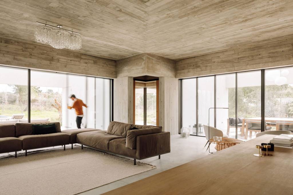 Sala de estar em cores terrosas, com paineis de vidro e revestimento do chão ao teto em cimento queimado