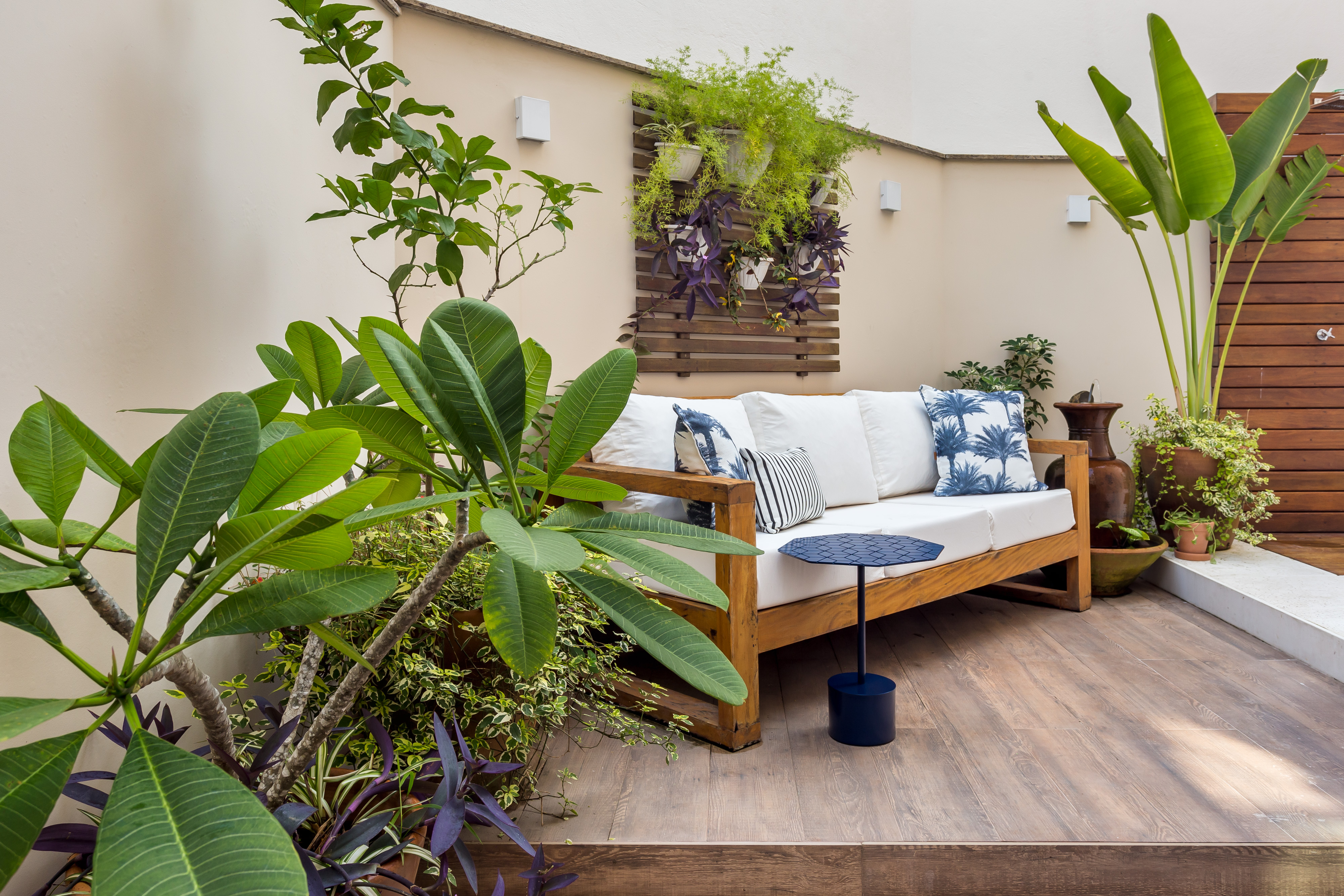 Área externa de um apartamento térreo com paisagismo que lembra quintal de casa, namoradeira branca com marrom e jardim vertical