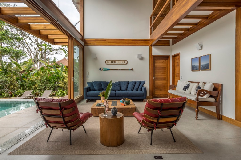 Casa com natureza ao redor, duas poltronas, um sofá e muita madeira