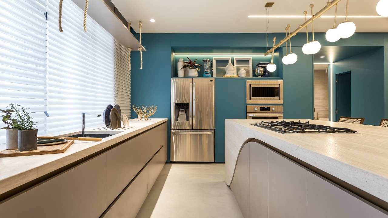 Cozinha com armários azuis, eletros em inox e bancada com armários cinzas embaixo, com cooktop