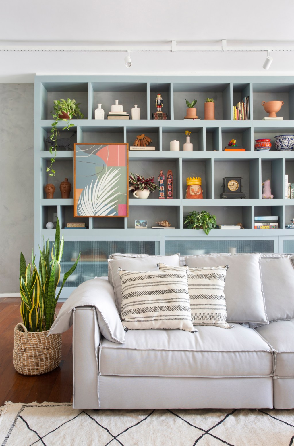 Sala de estar com estante nichada em azul e sofá de tom claro ao lado de um vaso de plantas