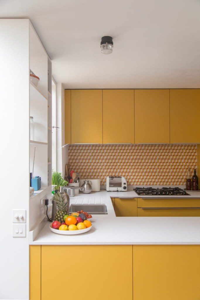 Cozinha em formato de u com marcenaria amarela e backsplash