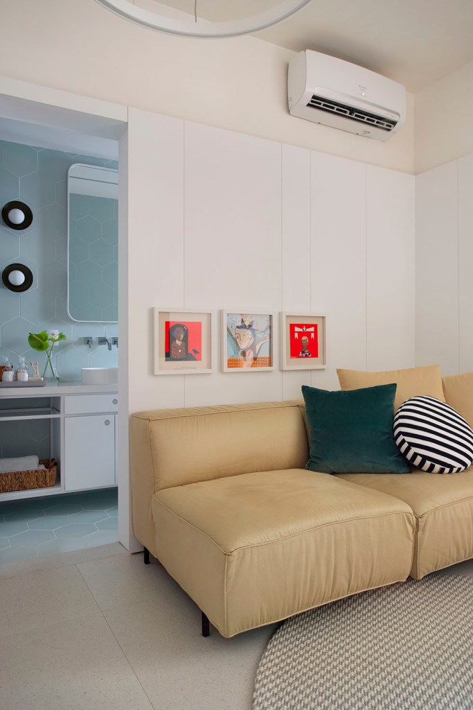 Apartamento de 40m2 em Copacabana assinado pelo arquiteto GUSTAVO PASSALINI _ foto 3 Sofá amarelo claro com três quadros quadrados pequenos acima do encosto. Almofada verde escura e almofada em forma de círculo branca e preta. Porta para o banheiro na lateral esquerda.