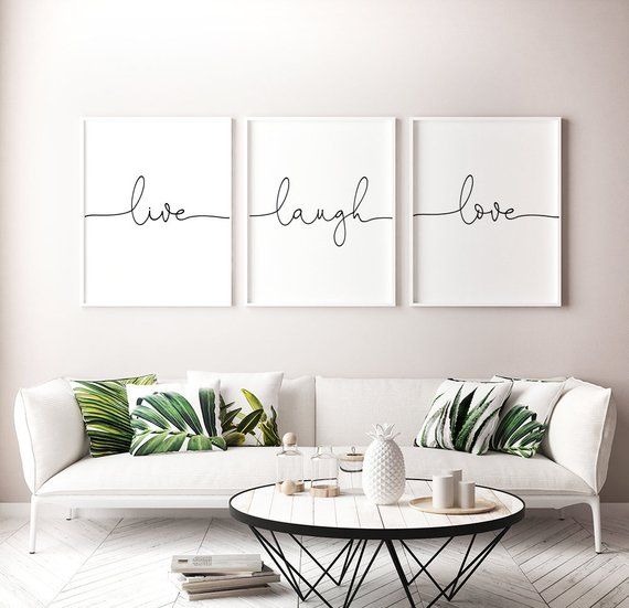 Living com sofá branco grande e almofadas com estampa de folhas. Na parede, quadros com as palavras Live Laugh e Love