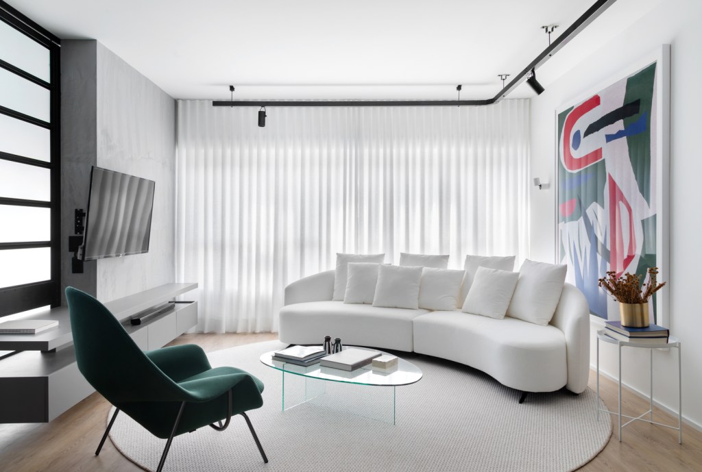 Sala de estar com piso de madeira e tapete redondo branco. O sofá, na mesma cor, é curvo e acompanha o movimento do tapete