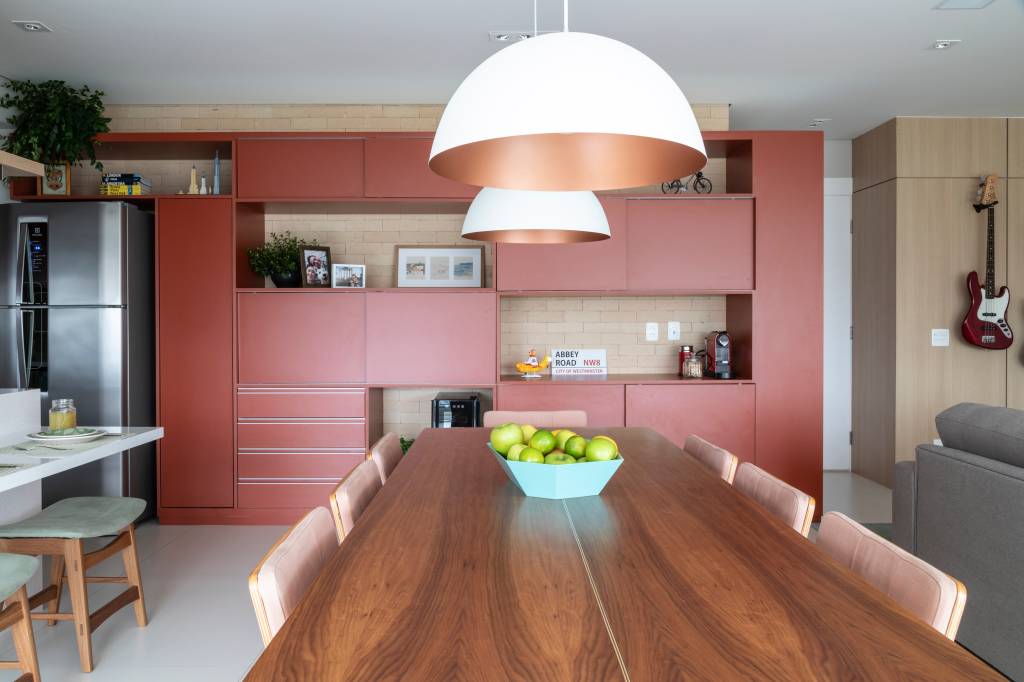 Armários na cor goiaba na parede do fundo, com uma mesa de jantar de madeira extensa em primeiro plano.