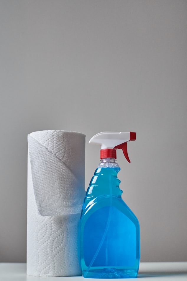 Embalagem em spray com liquido azul ao lado de rolo de papel toalha