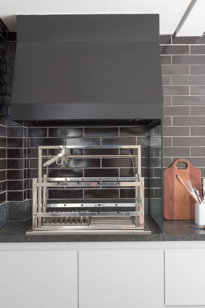 revestimentos-para-varanda-casa.com-Julia-Herman-6 Churrasqueira com grades prateadas elevadas, com coifa preta e revestimento de tijolinhos pretos brilhantes
