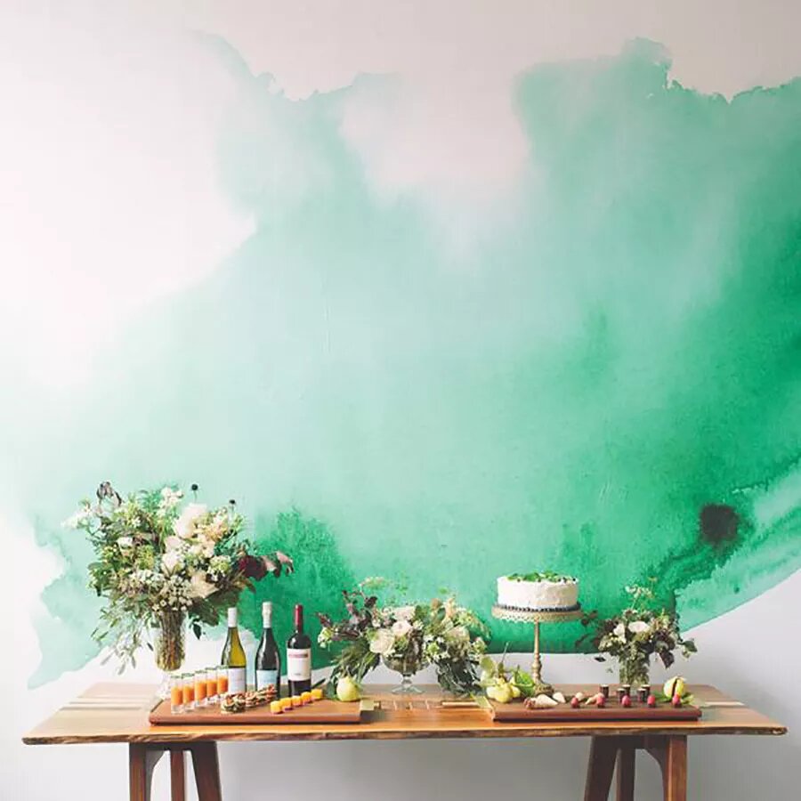 trends-anos-90-the-spruce-casa.com-4-anewall Parede branca com tinta verde aquarelada. À frente, um aparador de madeira, com vasos de flores