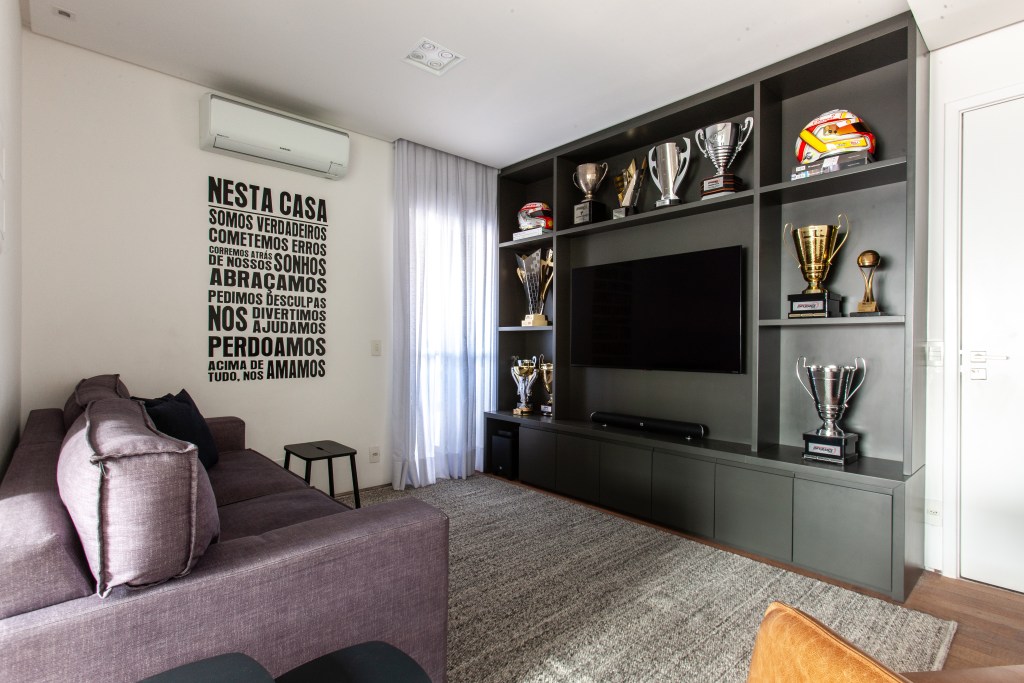 Sala de TV cujo painel é também uma estante que comporta troféus e capacetes de automobilismo