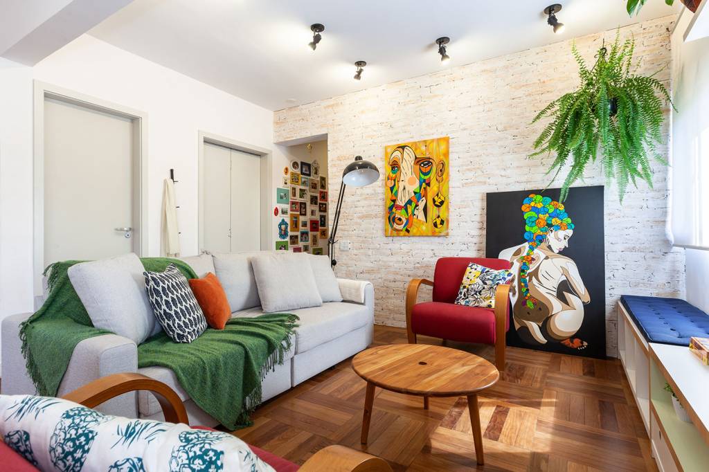 Sala de estar em tons neutro, com detalhes, como manta sobre o sofá, quadros na parede e poltrona coloridos