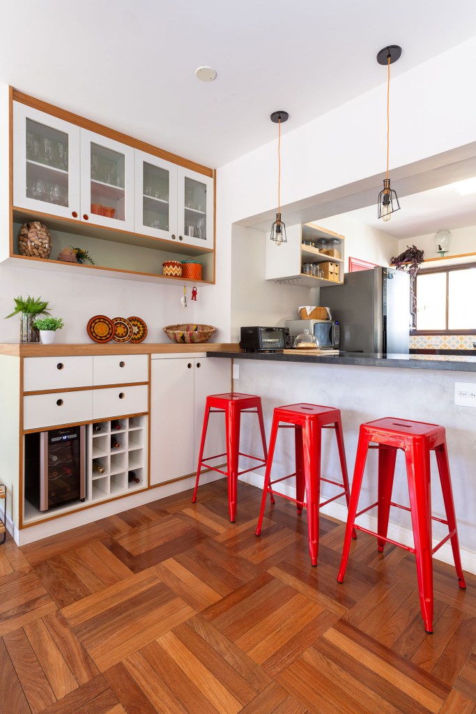 Cozinha em cores neutras, branco e madeira, com banquetas vermelhas