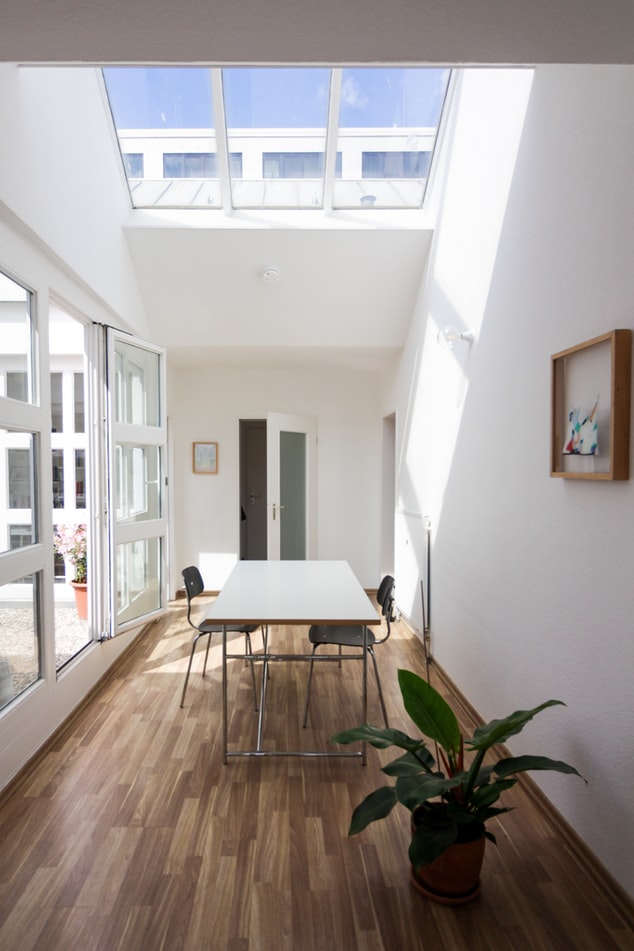 Sala com uma mesa e duas cadeiras, com piso de madeira, porta de correr de vidro e clarabóia no teto