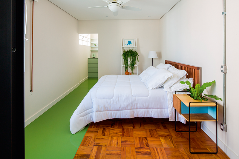O trecho de epóxi verde conecta o boxe ao closet. Ao lado da cama, o criado mudo faz parte da linha de mobiliário desenvolvida pelas arquitetas.