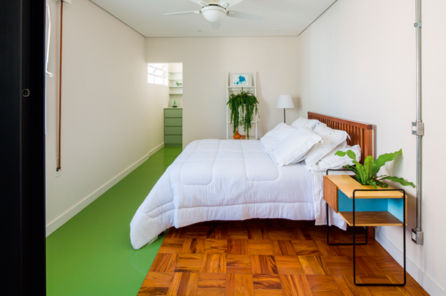 O trecho de epóxi verde conecta o boxe ao closet. Ao lado da cama, o criado mudo faz parte da linha de mobiliário desenvolvida pelas arquitetas.