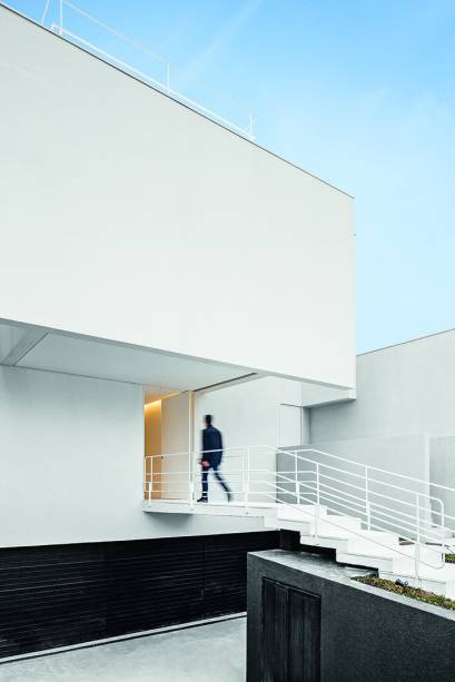 Empenas cegas como esta, da fachada, ocultam poços por onde o sol penetra na construção sem devassar a rotina dos moradores. Obedecendo o zoneamento, o recuo frontal mede 5 m – justamente o trecho no qual a escada vence o desnível. A pintura em preto faz com que o bloco de cima pareça flutuar.