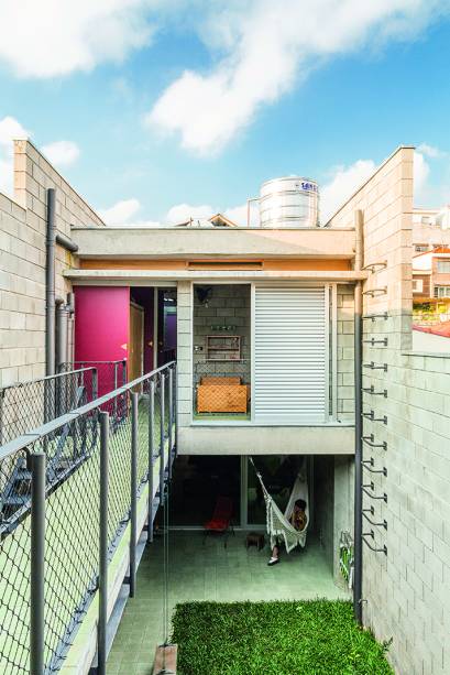 Nesta vista a partir dos fundos da casa, nota-se que a ligação com a edícula também se dá por uma passarela no piso superior. “Quando as garotas crescerem, uma delas certamente vai querer ocupar o quarto hoje dedicado aos hóspedes e o acesso pode acontecer por aí”, fala o arquiteto Chico Barros. Todo o trabalho de serralheria foi encomendado à Colombo Esquadrias.