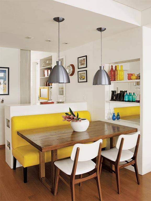 Nesta &aacute;rea de refei&ccedil;&otilde;es, um sof&aacute; amarelo de couro sint&eacute;tico &eacute; o destaque da decora&ccedil;&atilde;o. Uma mesa de cadeira maci&ccedil;a &eacute; servida por cadeiras, que acrescenta branco &agrave; combina&ccedil;&atilde;o quente. Uma estante embutida, com fundo espelhado, amplia visualmente este canto.