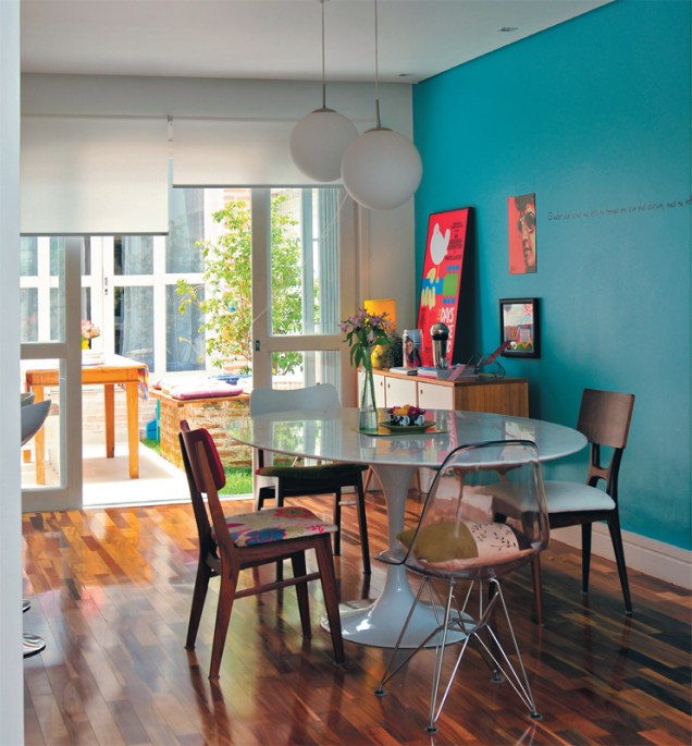 Na casa da designer Ana Maria Mouawad Queiroga, a mesa de jantar recebeu irreverentes cadeiras diferentes. A parede turquesa recebe a iluminação que vem pela porta de vidro (que substitui a janela) e uma cortina rolô controla a luminosidade do ambiente.