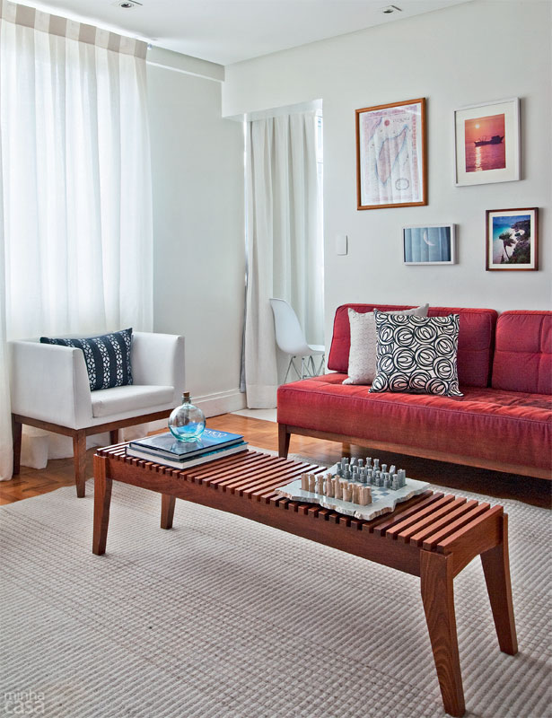 Sala de estar com sofá de veludo vermelho, mesa de centro retangular, parede branca com alguns quadros.
