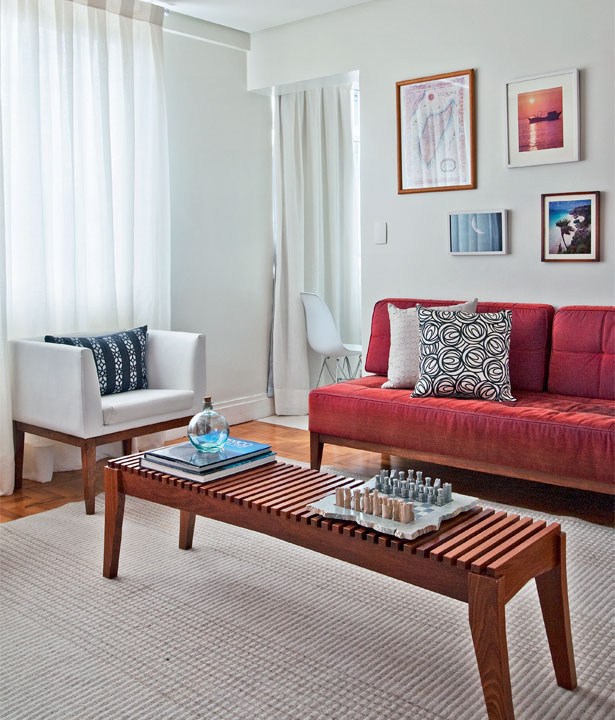 Sala de estar com sofá de veludo vermelho, mesa de centro retangular, parede branca com alguns quadros.
