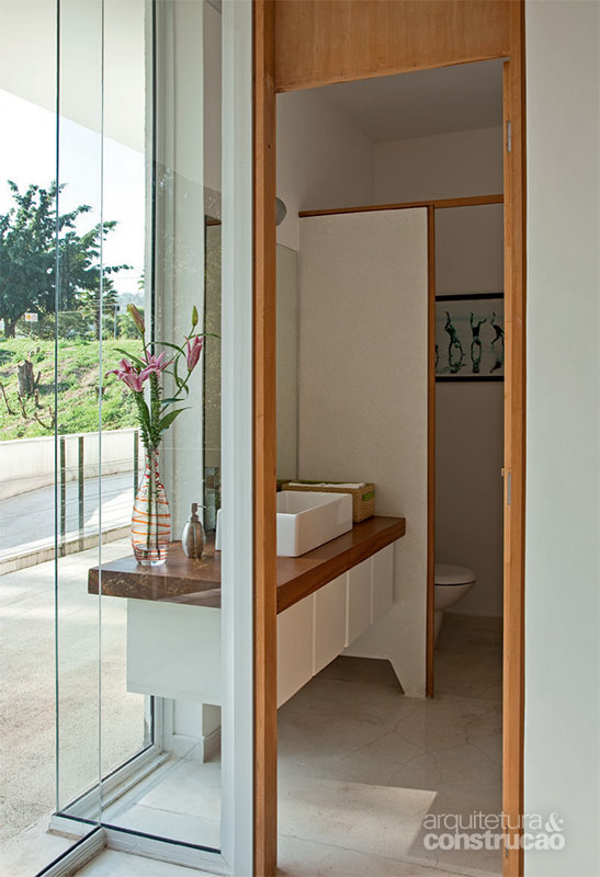 Dois painéis de vidro fixo, colocados em L, concedem luz natural e vista para o verde neste lavatório assinado pelo escritório Sidonio Porto Arquitetos Associados.