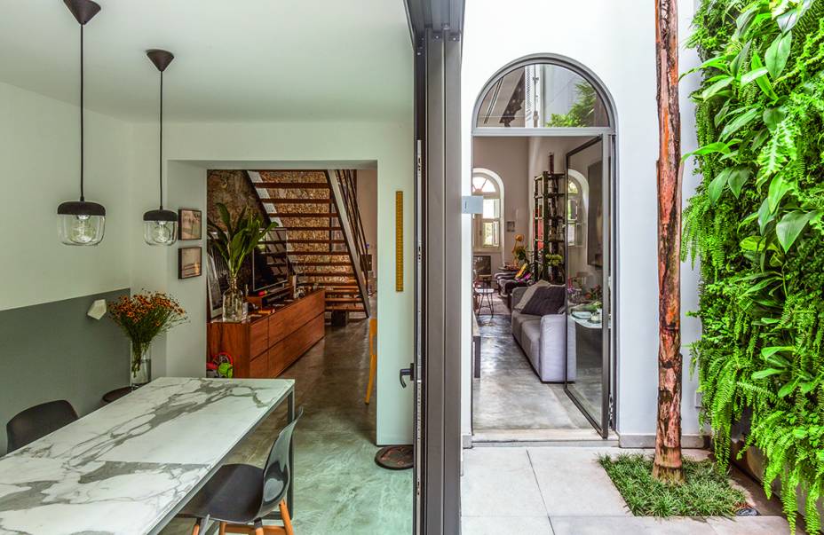 Além de separar a sala de jantar do pátio, onde ocorre a ligação entre os dois blocos, as esquadrias no tom grafite reforçam o estilo industrial da casa, pedido dos proprietários.