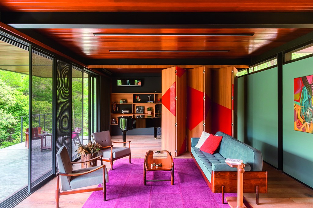 Madeira, aço e cimento desenham casa no topo de uma montanha Vigas e pilares metálicos ficam aparentes, fechados na varanda por meio de seis portas de correr de vidro e alumínio (com pintura eletrostática), seguidas de painéis com chapas de aço perfuradas (tingidas de esmalte sintético também preto e fosco) – para maior segurança. Execução da SJL esquadrias.