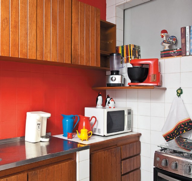 Jarras e açucareiros velhinhos conquistaram visual pop na cozinha após um banho de cor. Os azulejos brancos receberam uma camada de tinta vermelha, que contrastou com os armários de madeira e com a geladeira de inox. Projeto de Valentina Rocha.