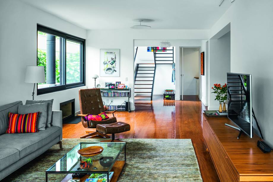 O cantinho da lareira (à esq., na foto) e o estar com TV ocupam este ambiente que se comunica, pela abertura à direita, com a sala de jantar conectada à cozinha. No piso, assoalho de perobinha (Felgueiras).