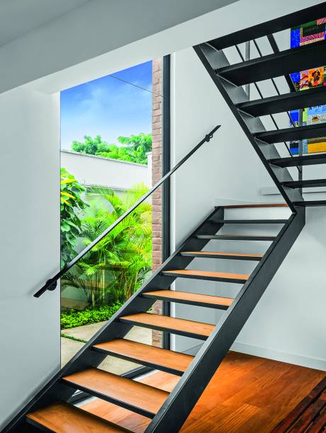 Pré-fabricada pela Plasmont, a escada metálica com pisadas de perobinha maciça chegou pronta à obra – seu desenho buscou viabilizar tecnicamente a largura ideal com o mínimo possível de componentes. LUZ DE CIMA A BAIXO:Preenchido com duas chapas fixas de vidro laminado, o rasgo de 1,45 x 5,80 m liga visualmente os dois pavimentos e deixa entrar mais claridade.