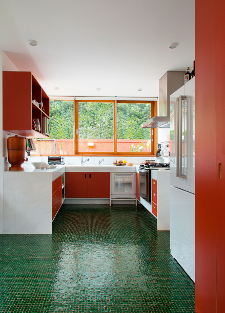 Agora voltada para a rua, a cozinha repete, no piso de mosaico de vidro e na marcenaria sob medida, o verde e o vermelho tão presentes no jardim. A bancada emprega mármore espírito santo (DMX2 Mármores e Granitos). Toda a caixilharia é de freijó. Projeto: André Vainer Arquitetos.