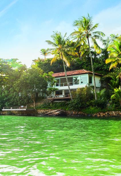 Entre o verde do mar da Praia de Santa Tereza e o da vegetação nativa, surge a casa com seus tons de branco e azul.