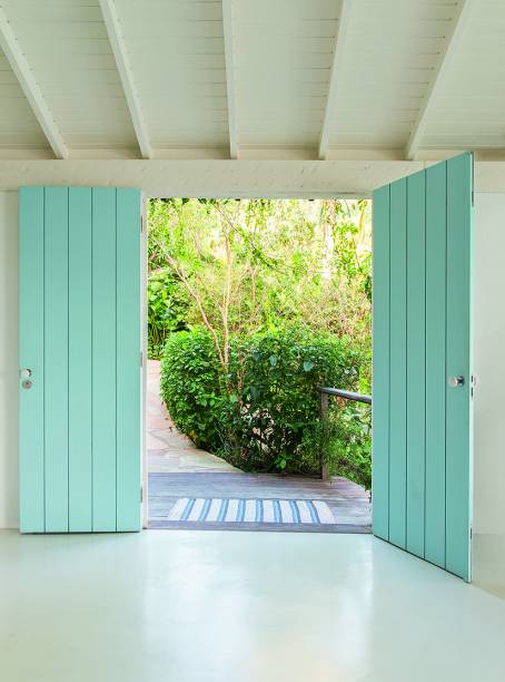 Na entrada, a porta dupla de madeira maciça com réguas verticais garante o acesso ao pavimento principal, onde ficam as salas e a suíte maior, além de um quarto de hóspedes. Amplo e sem pilares aparentes, o ambientesocial funciona como uma grande varanda voltada para a mata e o mar, cercada de painéis de vidro.