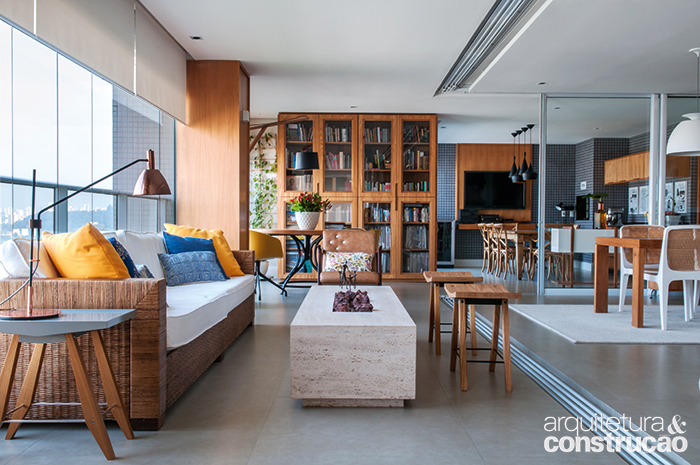 O arquiteto Rafael Leão, do Studio 3.7 Arquitetura e Interiores, converteu a varanda do apartamento paulistano em um ambiente polivalente, com cinco funções. Todas as microambiências conversam de forma harmônica e se integram ao living, separado pelas portas de correr de vidro originais, mantidas. Para tanto, o piso e o forro foram nivelados e a iluminação, uniformizada, com lâmpadas dicroicas pontuais. A marcenaria (Marcenaria Silva & Suzuki), toda de freijó, se encarrega de reforçar a unidade. Assim, o trecho em L de 66 m² ganhou sala com lareira, além de um canto com churrasqueira e áreas de trabalho, descanso, estudos e jogos. A lareira a gás (LCZ Lareiras) ocupa o centro da mesinha de travertino romano bruto (Mont Blanc Mármores), de 35 x 60 x 200 cm.