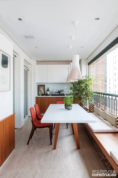 O apartamento recém-comprado ostentava uma varanda generosa, com quase 11 m de comprimento. O problema era a largura: apenas 2,5 m. Os novos donos queriam que o espaço comportasse uma mesa de jantar e uma sala de estar, mas a estrutura não ajudava. A solução dada pelo arquiteto Felipe Hsu foi instalar um banco de freijó junto ao guarda-corpo, ligando as duas extremidades do terraço e assegurando unidade ao ambiente. Piso de travertino romano bruto.