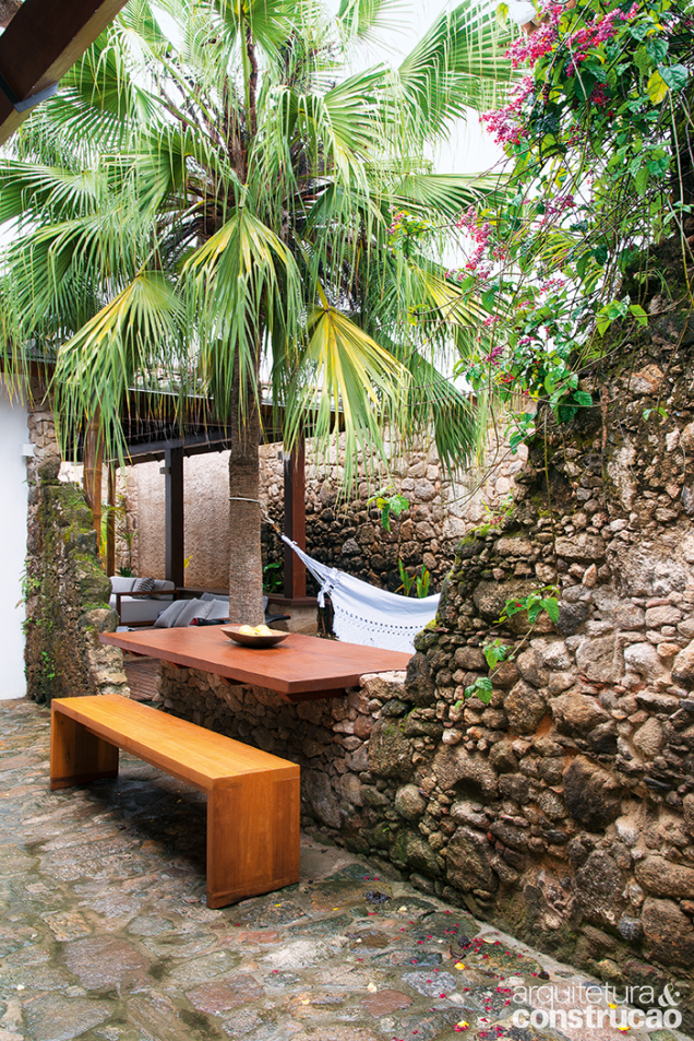 O arquiteto encaixou uma mesa para refeições ao ar livre (Marcenaria da Mangueira) no muro de pedra moledo parcialmente destruído. O arquiteto encaixou uma mesa para refeições ao ar livre (Marcenaria da Mangueira) no muro de pedra moledo parcialmente destruído.