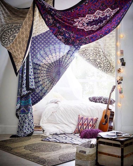 Sala com cama e tecidos coloridos pendurads