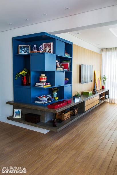 Com um rack de concreto em L, o arquiteto Bruno Reis e a designer Helena Kallas, do Mandril, deram unidade à varanda do dúplex, incorporada como canto de TV à área social, logo à frente. “Uma peça reta denunciaria a integração”, justifica Bruno. Coberta com nata de cimento queimado, essa base fixa se completa com o painel de madeira e os módulos laqueados de azul.
