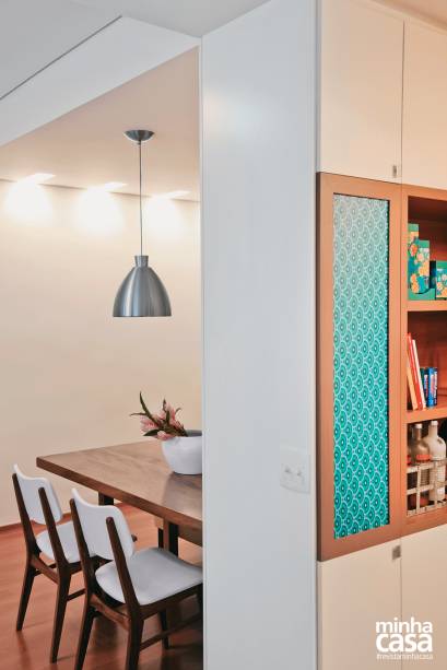 As arquitetas aproveitaram o “avesso”do nicho espelhado (no lado do jantar) para inserir prateleiras para caixas, livros e bebidas. Acima e abaixo dessa estante – ladeada por uma inusitada luminária embutida, feita de chapa de acrílico coberta de adesivo vinílico com estampa verde –, há discretos armários. Projeto das arquitetas Isabella Lucena e Joanna Fraga.